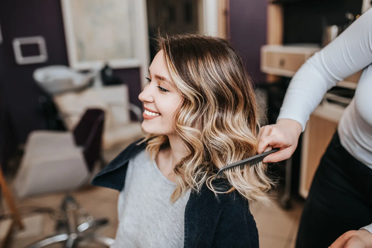 Eine junge Frau mit welligem blonden Haar lacht entspannt beim Friseurbesuch