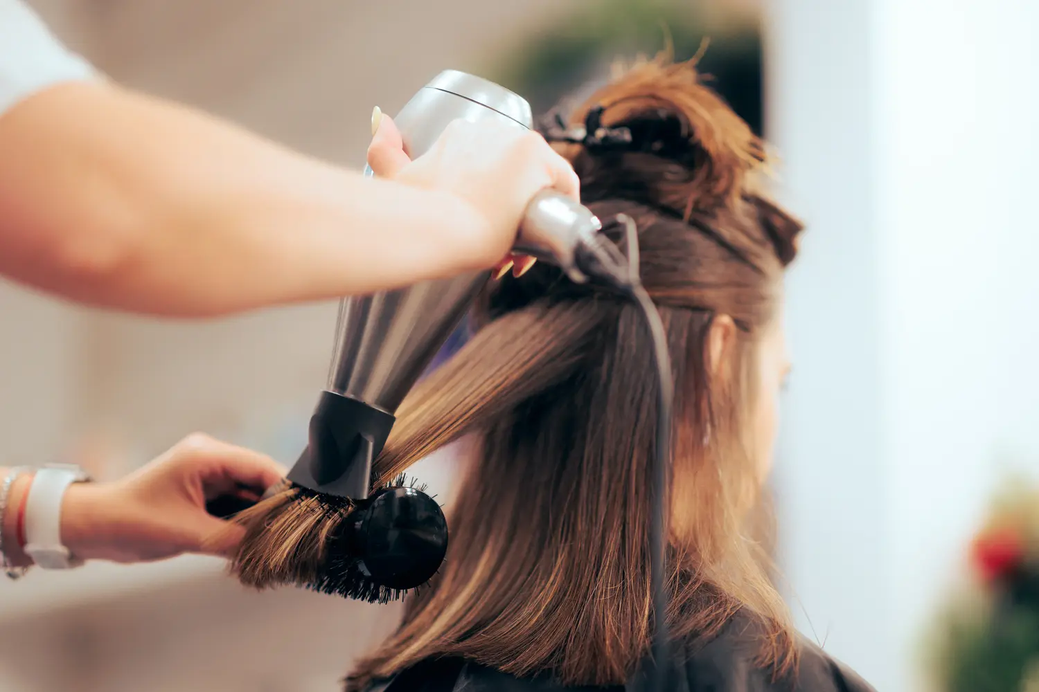 Eine Frau mit langen braunen Haaren wird im Salon frisiert und wirkt entspannt